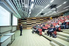 man-standing-in-front-of-people-sitting-on-red-chairs-1708936.jpg